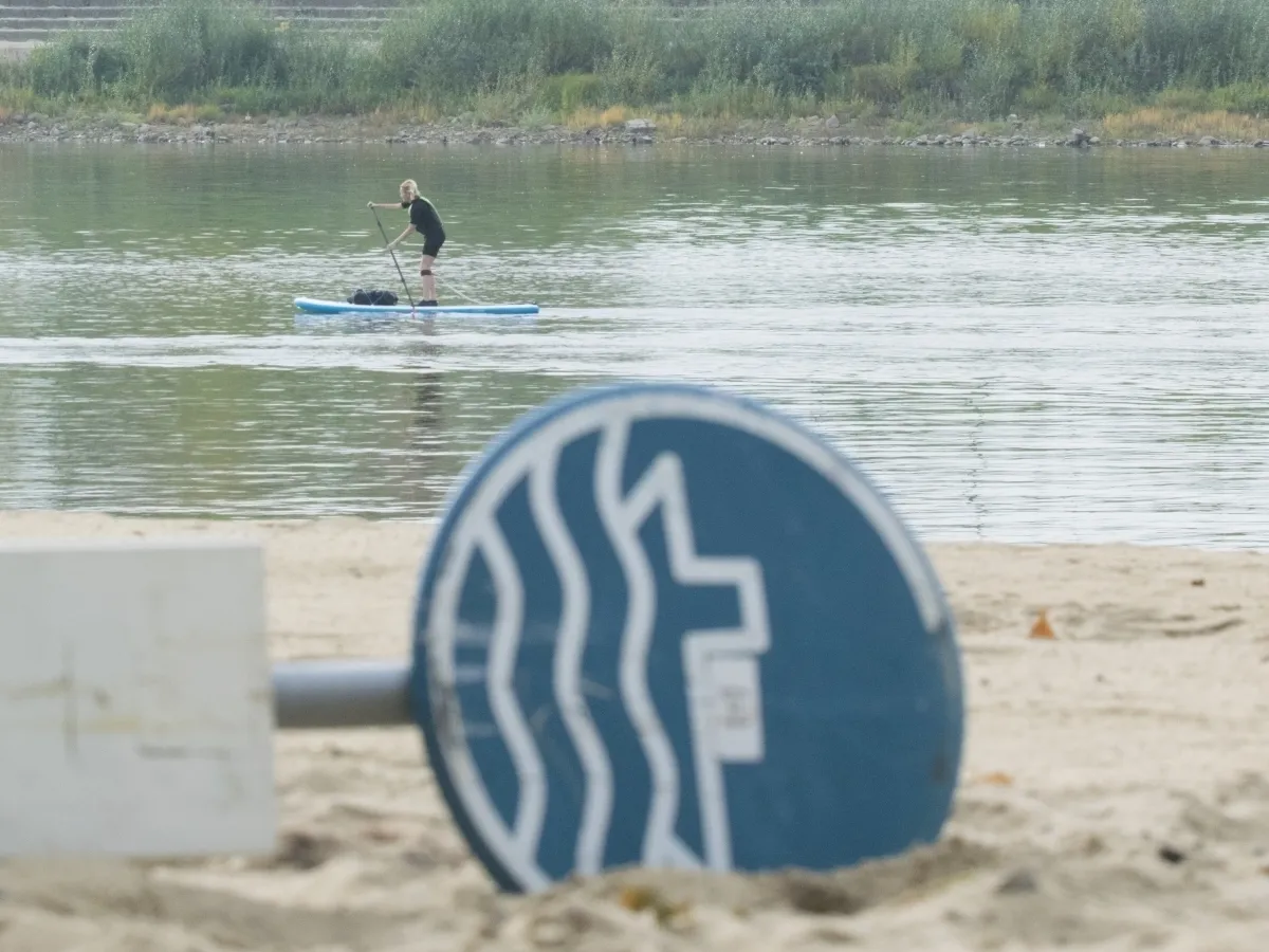 Paddleboarder on a river seen past a fallen blue swimming sign